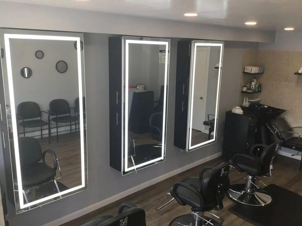 Inside the salon: three tall mirrors framed in white light, black styling chairs and a shampoo bowl