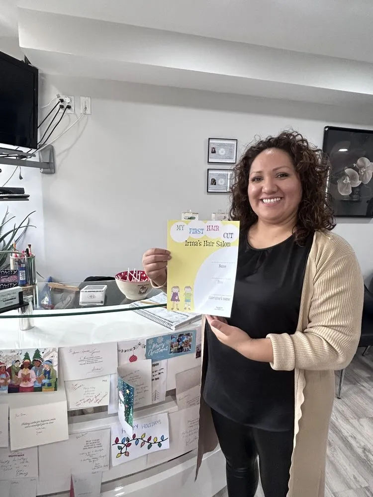 A stylist at the front desk holding up a yellow My First Hair Cut certificate from Irma's Hair Salon