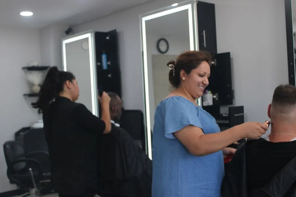 Two stylists cutting clients’ hair at the lit mirror stations
