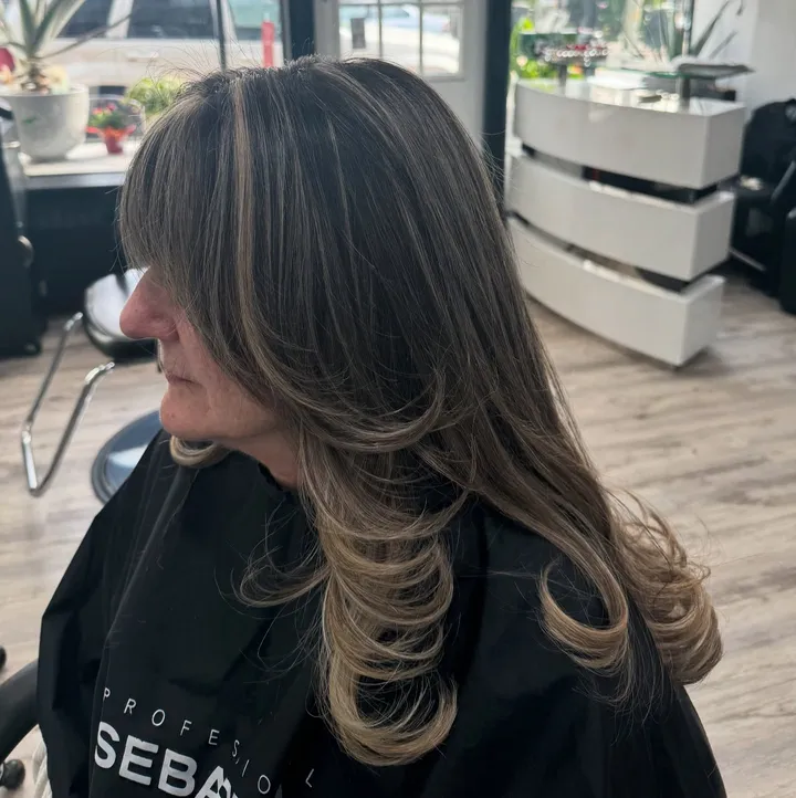 Long layers with curtain bangs and face-framing blonde highlights, from the side