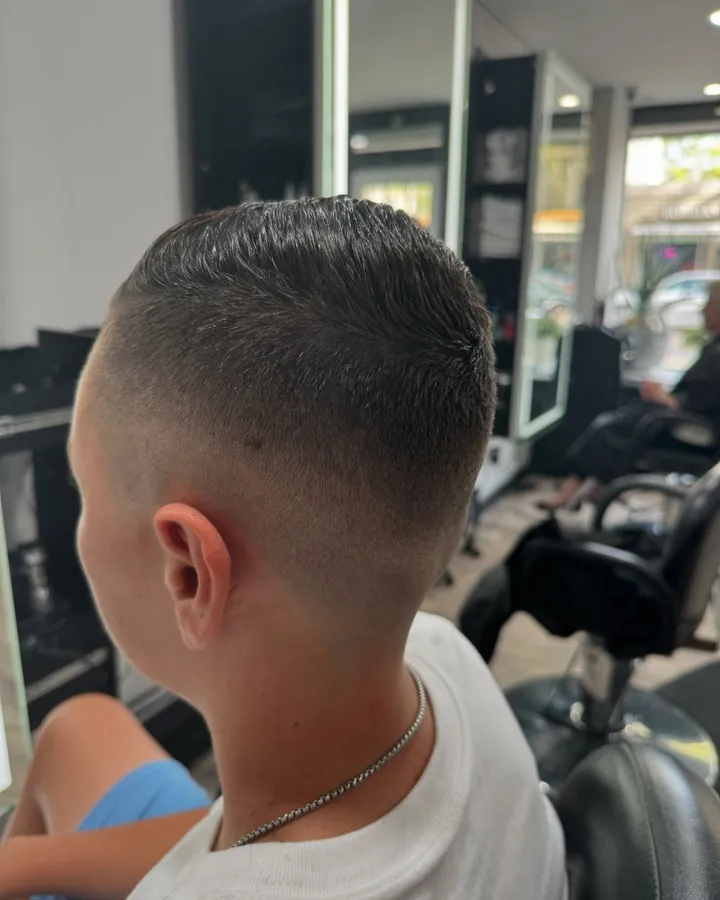 A boy’s skin fade with a short, combed-back top, seen from behind