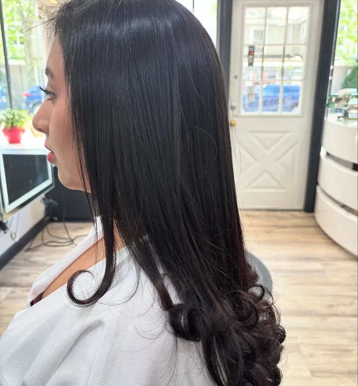 Long dark brown hair, smooth at the crown and curled at the ends, from the side